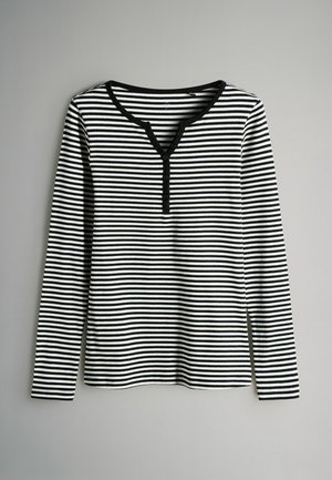 Dlhý rukáv pruhovaný top v čiernej a bielej farbe, s výstrihom do V a gombíkovými detailmi, ribovanou textúrou a rovnou spodnou časťou.