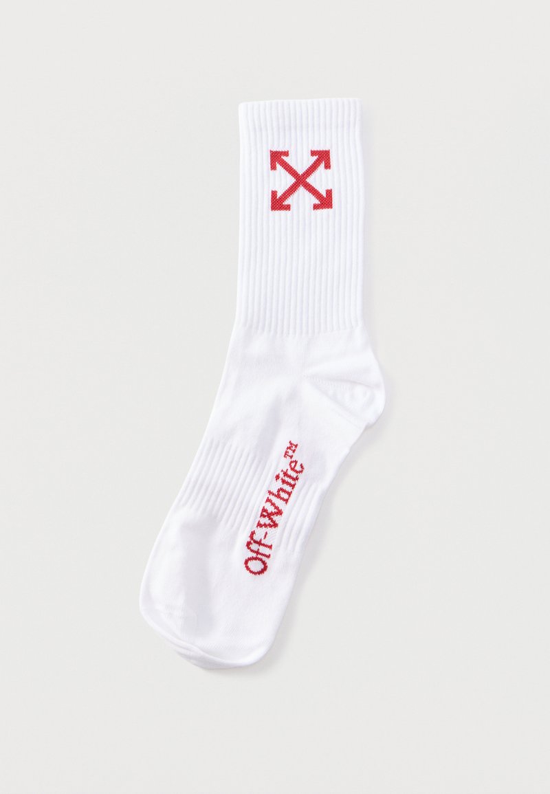 Chaussette blanche côtelée avec texte rouge Off-White sur le pied et un logo rouge à quatre flèches près du bord supérieur.