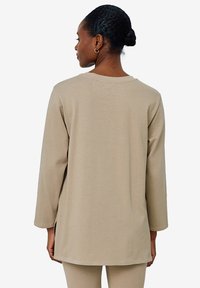 Beige Langarmshirt aus weichem Baumwollmaterial, mit Rundhalsausschnitt, leicht oversized Schnitt, flachen Nähten und seitlichen Schlitzen für mehr Bewegungsfreiheit.