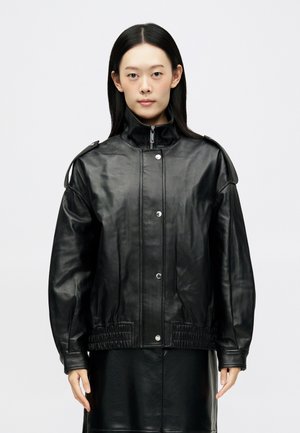 Veste en cuir noir avec un col haut, des boutons-pression et une taille élastiquée. Elle possède des détails rembourrés aux épaules et des manches longues.