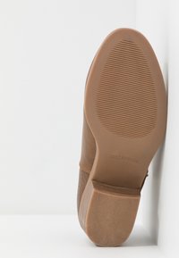 Chaussure marron avec panneaux latéraux texturés, tige en cuir lisse, semelle en caoutchouc et rainures horizontales sur le dessous pour l'adhérence.
