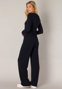 Langemouwen marineblauw top gecombineerd met hoge taille marineblauwe wijde broek. Zachte stof, minimale stitching en subtiele achterzakken. Sportieve witte schoenen.