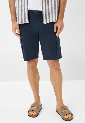 Navy cargo shorts with side pockets, lightweight fabric, and stitched hem. Paired with brown slide sandals. Striped shirt visible above.