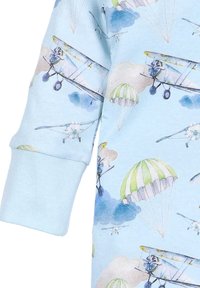 Jasnoniebieska tkanina z wzorem vintage samolotów i spadochronów. Gładka struktura z prążkowanymi mankietami. Styl akwareli.