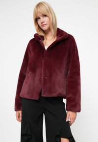 Burgundia faux karusnahast jakk, millel on kapuuts, lühike disain ja nööbid. Pehme tekstuur ja laiad varrukad mugava istuvusega.