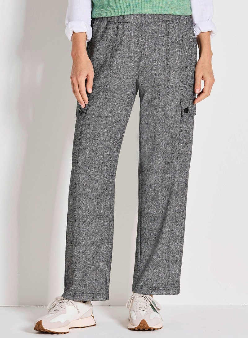 Grijze, gestructureerde cargobroek met een losse pasvorm, voorzien van zijzakken en een zwarte knoopdetails. Gepaard met witte sportschoenen.