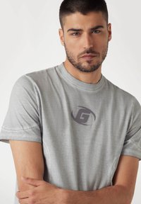 Harmaa crew-neck t-paita, joka on valmistettu pehmeästä kankaasta. Siinä on lyhyet hihat ja tummanharmaa logo edessä. Yksinkertainen design ja rento istuvuus.