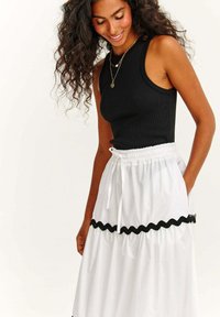 Schwarzes ärmelloses, geripptes Top kombiniert mit einem weißen Rock mit elastischem Bund und schwarzem, gewelltem Saum. Helle, glatte Stoffstruktur.