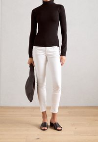 Svart polotröja, vita slim-fit jeans, svarta sandaletter, håller en svart väska. Svala texturer, enkel design, modern look.