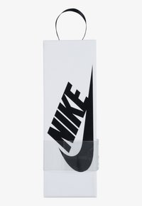 Fehér dobozos csomagolás, kiemelkedő fekete Nike logóval. Átlátszó műanyag borítás az elején. Fekete szalagfogó a tetején. Egyszerű háttér.