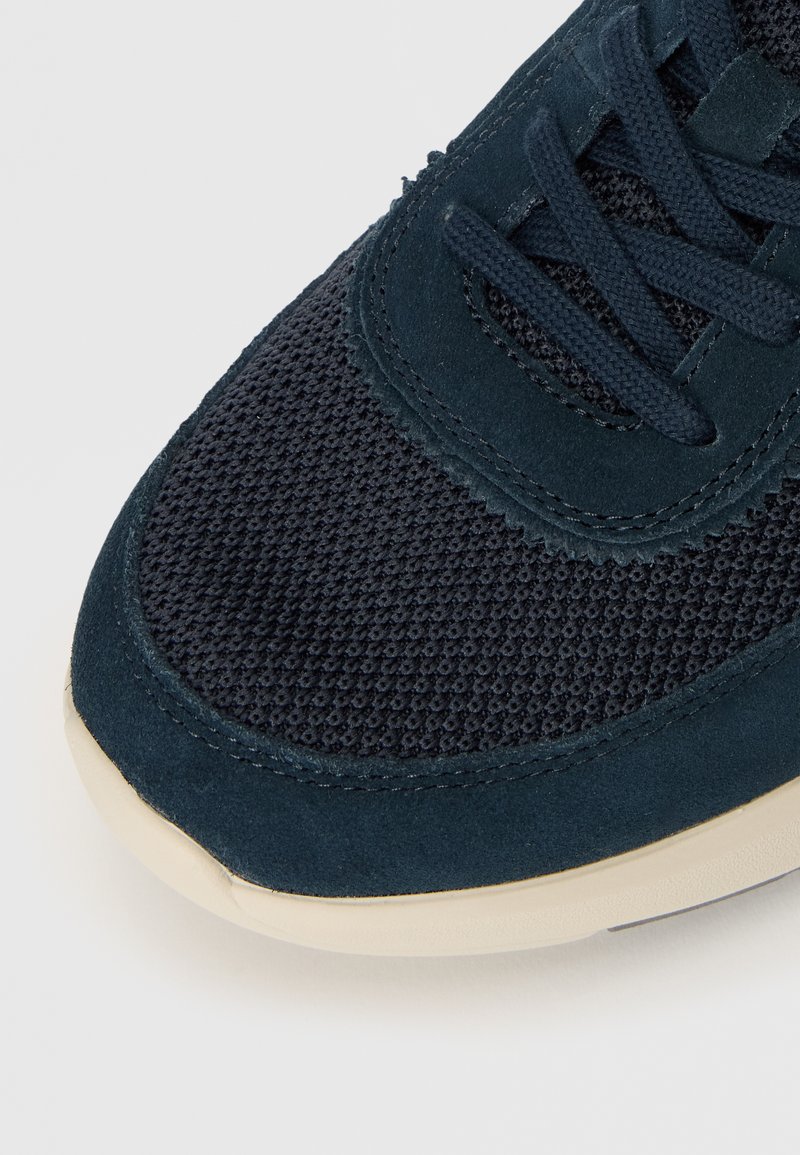 Ciemnoniebieskie sneakersy z siateczkowej tkaniny i zamszowej tekstury. Posiadają dopasowane sznurowadła oraz jasną gumową podeszwę. Zaokrąglony design nosa.