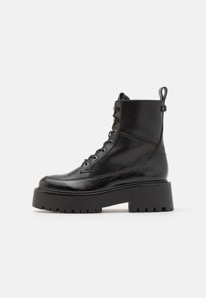 Botas de cuero negro hasta el tobillo con punta redonda, parte delantera con cordones, ojales reforzados y suela de plataforma gruesa. Presilla trasera para ponerlas con facilidad.