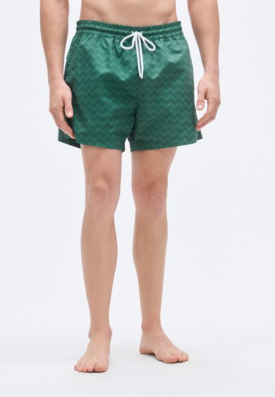 Shorts de bain verts présentant un motif en chevron, une taille élastique avec cordon de serrage, et un tissu lisse et léger.