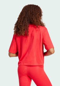 Röd bomulls-topp med korta ärmar, avslappnad passform och rund halsringning, tillsammans med matchande röda leggings, som visar en mjuk textur och avslappnad design.