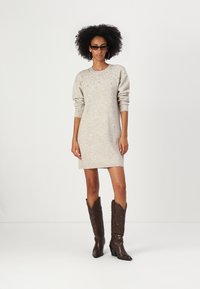 Abito maglione grigio chiaro in maglia con maniche lunghe, scollatura rotonda e decorazioni sottili; abbinato a stivali cowboy marrone scuro.