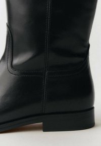 Svart läderboots med en slät yta, med en sydd sömdesign och en låg blockklack.