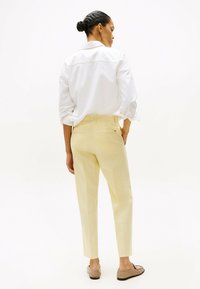 Lichtgele, op maat gemaakte broek met een slanke pasvorm en twee achterzakken, gecombineerd met een wit, knoopsluiting shirt en bruine platte schoenen.