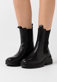 Botines negros de tobillo hechos de cuero liso, con paneles laterales elásticos, tiradores y suelas de goma texturizadas para mayor agarre.