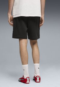 Shorts de sport noirs avec poches latérales, texture lisse et coupe décontractée, associés à des chaussures de sport rouges et des chaussettes blanches mi-mollet.