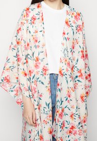 Kimono floral en tissu transparent, avec un fond blanc orné de fleurs roses et orange, des manches larges et une coupe ample et fluide.