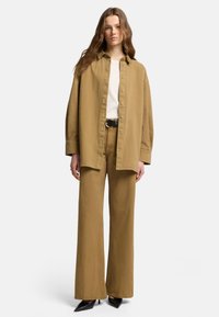 Una camicia button-up over-size abbinata a pantaloni larghi dello stesso colore; presenta una t-shirt bianca sotto e una cintura nera. Tacchi a punta neri.
