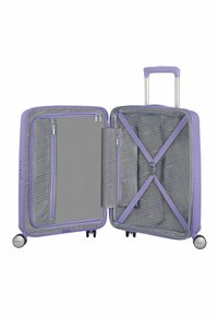 Valigia rigida viola con superficie testurizzata, doppie compartimenti, interno grigio, tasche con cerniera e cinghie incrociate per fissare gli oggetti.