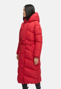 Manteau long rembourré rouge avec capuche, taille ceinturée et texture matelassée. Présente un design élégant et deux poches latérales pour plus de praticité.