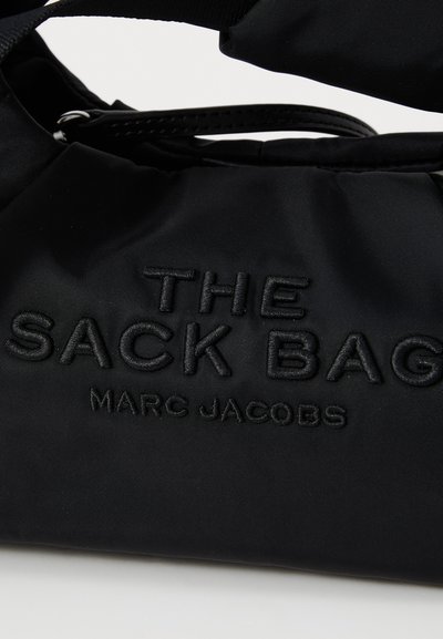 Bolsa de nylon negra con texto en relieve que dice "THE SACK BAG" y "MARC JACOBS". Presenta un diseño simple y una textura suave.