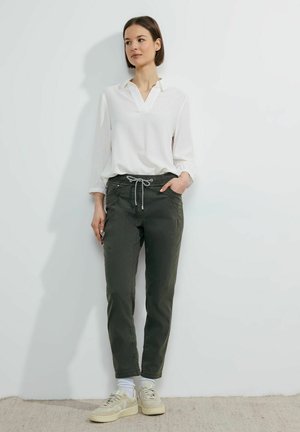 Bílá košile s dlouhým rukávem a límečkem, spárovaná s tmavě zelenými kalhotami na gumu v pase. Světlá obuv, slim fit, hladký materiál, s detaily na šňůrku.