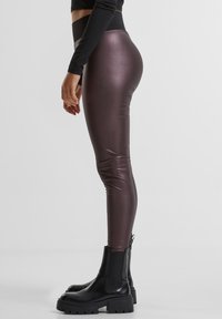 Højttaljede, metalliske burgunderfarvede leggings med en glat tekstur, kombineret med chunky sorte ankelstøvler med elastiske sidepaneler.