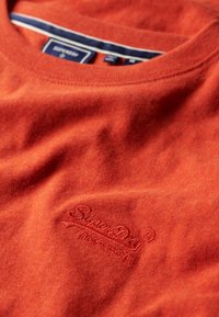 Orange crewneck sweater med "Superdry" broderet logo og japanske tegn på brystet, med et navyblåt og hvidt stribet krave-label.