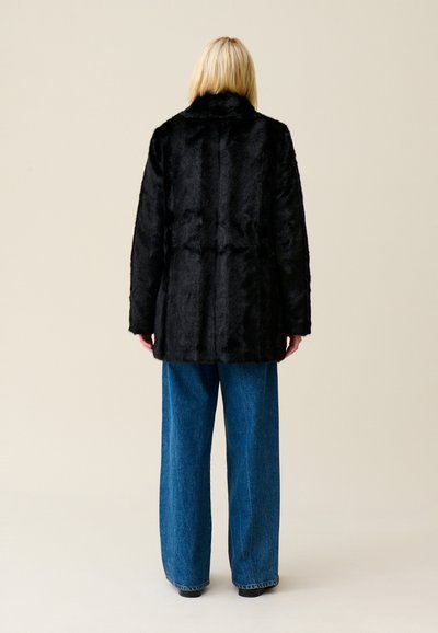 Cappotto in pelliccia sintetica nera con ampio colletto e maniche lunghe, abbinato a jeans blu di denim a vita alta e larghi. Texture liscia, design che offre una copertura completa.