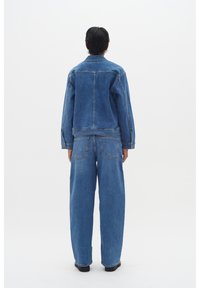 Denim jakna in široke hlače iz srednje modrega denima. Jakna ima klasičen kroj z delom šivov, medtem ko imajo hlače zadnje žepi.