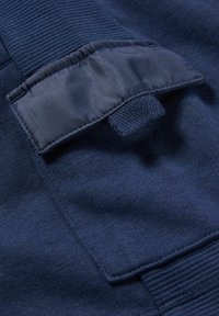 Gros plan sur un tissu bleu marine avec un poignet côtelé texturé et une poche à rabat sécurisée par une languette tricotée sur un vêtement.