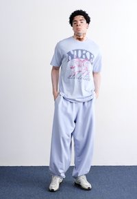 Lysblå Nike t-shirt med et rødt grafisk design, parret med matchende lysblå løstsiddende bukser og grå sportsko.