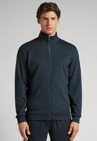 Chaqueta navy con cremallera y alto cuello, puños y cinturilla de canalé. Tejido suave con un diseño minimalista y un sutil detalle de costura.