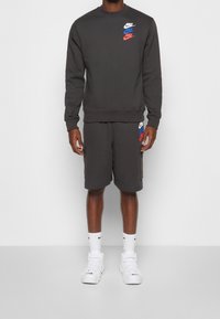 Grå sweatshirt med röda, blå och vita Nike-logotyper på bröstet, kombinerad med matchande shorts. Vita sneakers och strumpor fulländar outfiten.