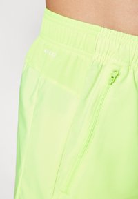Neon-grüne Sportshorts mit einem elastischen Bund, seitlicher Reißverschlusstasche und glattem, leichtem Material. Markenlogo am Bund aufgedruckt.