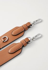 La cinghia in pelle marrone presenta accessori in metallo argento, un D-ring e dettagli a linguetta. Superficie liscia con cuciture a contrasto lungo i bordi.