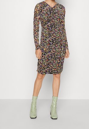 Robe à manches longues florale avec une base noire, des fleurs multicolores, des détails froncés et une silhouette ajustée. Associée à des bottines vertes brillantes.