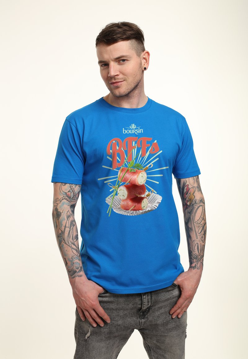 Modrá bavlněná tričko s nápisem "BFFs" a grafikou sushi s pažitkou na bílé talíři. Model nosí otrhané šedé džíny.