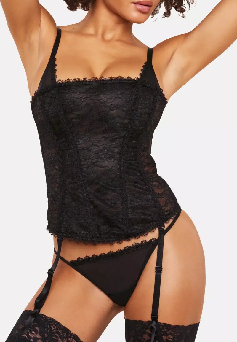 Black lace corset with adjustable straps, featuring scalloped edges and a fitted design. Paired with a black thong and lace-top stockings.