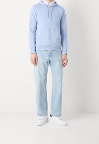 Světlě modrá mikina s kapucí, přední kapsou a stahovací šňůrkou, doplněná světlými džínami s přímým střihem a bílými teniskami. Jednoduchý, ležérní outfit.