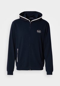 Sudadera azul marino con cremallera, hecha de tela suave, con ribete blanco contrastante alrededor de la capucha, los bolsillos delanteros y un logo bordado.