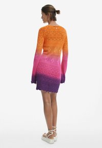 Vestito lavorato a maglia con colori sfumati dall'arancione al viola, caratterizzato da una vestibilità morbida, maniche lunghe e dettagli a bordi ondulati.