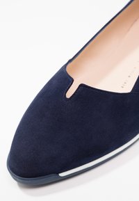 Ballerines en suède bleu marine avec un design découpé à l'avant et un fin accent blanc le long de la semelle. Doublure intérieure lisse.