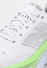 Witte sportschoen met een glad bovenwerk, versterkte hiel en een groene tussenzool. Voorzien van mesh ventilatie, platte veters en geometrische patroonaccenten.