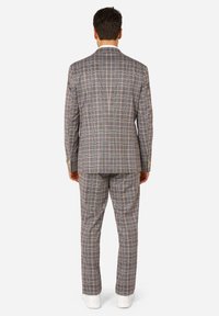 Traje de cuadros gris con un diseño ajustado y un patrón a rayas en tonos claros y oscuros, combinado con zapatillas blancas.