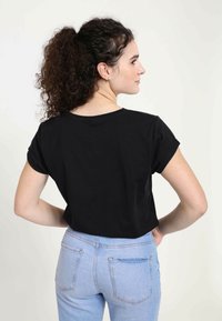 Sort kortærmet t-shirt med en afslappet pasform. Båret sammen med lyseblå high-waisted jeans. Simpel, glat tekstur og uden detaljeret design.