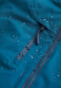Vattentålig teal-färgad jacka med synliga vattendroppar, med dragkedjestängning och texturerad yta med en slät finish.